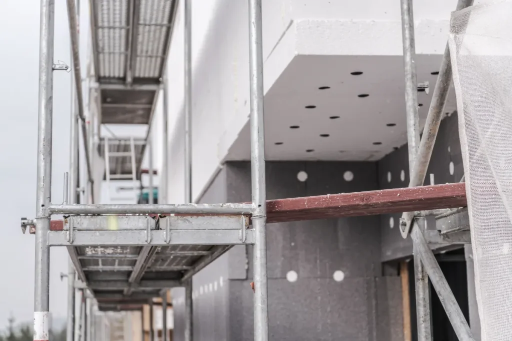 Baustelle mit Gerüst und Fassadensanierung, bei der Dämmmaterial an der Wand angebracht wird