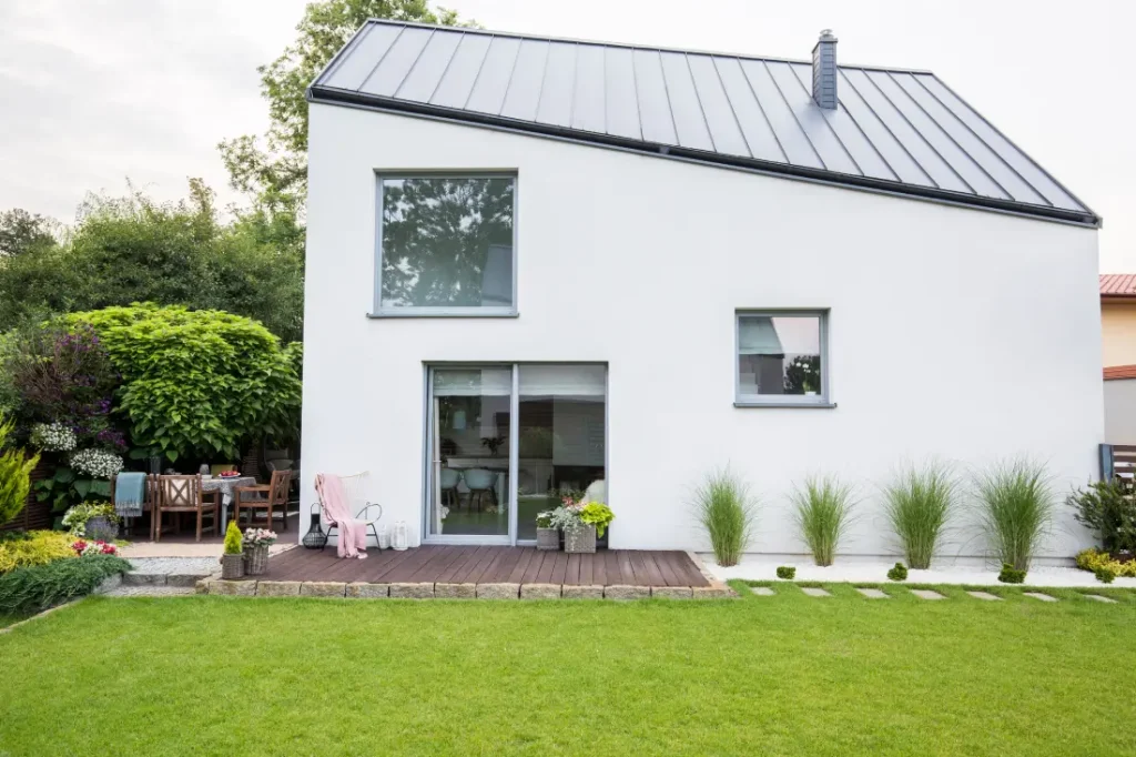 Außenansicht eines modernen Hauses mit einem großen Schiebetürfenster, das auf eine Terrasse und einen Garten führt – ein Beispiel für das Erneuern von Fenstern, um den Wohnbereich mit der Außenwelt zu verbinden und mehr Licht zu nutzen.